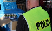 policjant w kamizelce odblaskowej z napisem Policja, który przy kartonach trzyma paczki papierosów