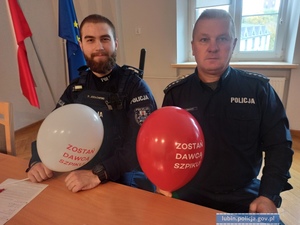 Policjanci siedzą przy biurku i mają balony z napisami promującymi zostanie dawcą szpiku