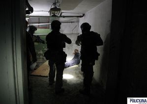 Stacja „Uczony”. Zadanie: uwolnić i ewakuować rannych zakładników z zaminowanych pomieszczeń. Trzech kontrterrorystów stoi tyłem i patrzy na mężczyznę, który leży pod ścianą