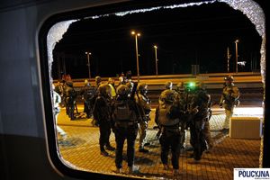 Widok na peron i policyjnych kontrterrorystów przez wybitą szybę w pociągu