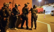 pięciu uzbrojonych policjantów stoi przy ścianie budynku