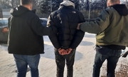 dwaj nieumundurowani policjanci prowadza zatrzymanego mężczyznę zakutego w kajdanki