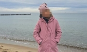 dziewczynka w różowej czapce na głowie i różowej kurtce stoi na plaży