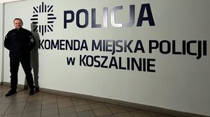 asp. Daniel Maciążek stoi na tle ściany z napisem Komenda Miejska Policji w Koszalinie