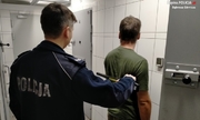 Zatrzymany Mężczyzna stojący tyłem, przeszukiwany przez umundurowanego policjanta detektorem do metalu