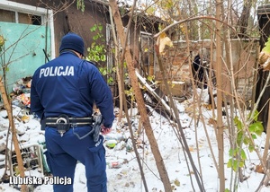 policjant w trakcie poszukiwań przy starym, opuszczonym budynku wśród zarośli
