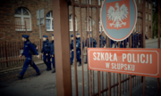 grupa policjantów maszeruje, na pierwszym planie tabliczka na bramie z napisem Szkoła Policji w Słupsku, a nad nim godło Polski