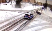 Pokryta śniegiem ulica. Radiowóz policyjny i jadący przed nim samochód osobowy