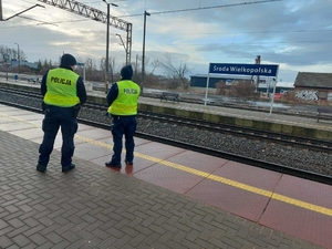 Dwóch umundurowanych policjantów patrolujących perony kolejowe.