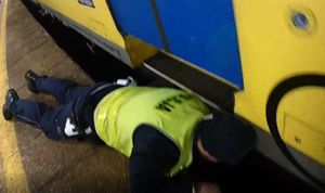 policjant pomaga mężczyźnie, który wpadł między peron, a jadący pojazd szynowy