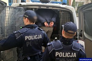 Zatrzymany mężczyzna prowadzony przez policjantów  do radiowozu