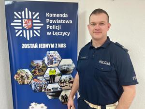 umundurowany policjant stoi przy banerze Komendy Powiatowej Policji w Łęczycy