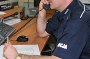 umundurowany policjant siedzi przy biurku i rozmawia przez telefon stacjonarny