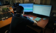 Zdjęcie przedstawia umundurowanego policjanta, który siedzi przed komputerami