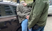 policjant z zatrzymanym zakutym w kajdanki przy samochodzie