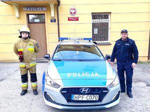 policjant i strażak stoją przy radiowozie policyjnym
