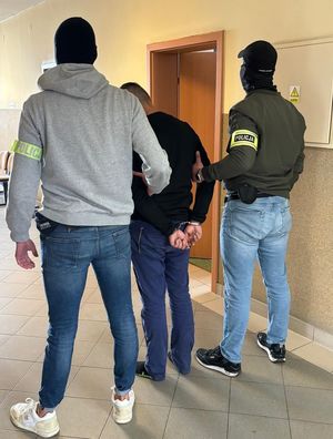 policjanci prowadzą korytarzem zatrzymanego mężczyznę