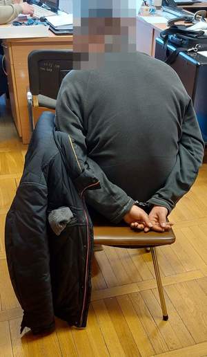 Zatrzymany mężczyzna siedzi na krześle skuty kajdankami podczas przesłuchania.