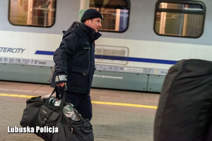 Policjant niosący torbę na peronie kolejowym.
