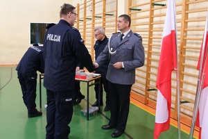 Sala gimnastyczna Oddziału Prewencji Policji w Łodzi, uroczystość ślubowania nowo przyjętych policjantów, oficer wręcza legitymację służbową nowemu policjantowi.