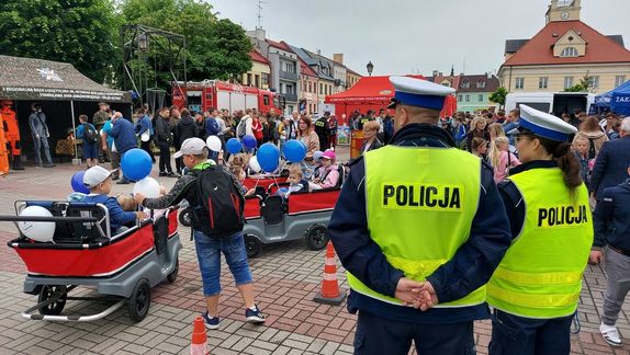 Policjanci stoją tyłem w tle uczestnicy pikniku mundurowego na placu Tadeusza Kościuszki.