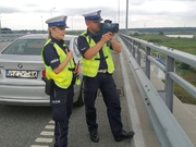 Policjantka i policjant w kamizelkach podczas działań mierzą odległości między jadącymi pojazdami za pomocą specjalnego urządzenia.