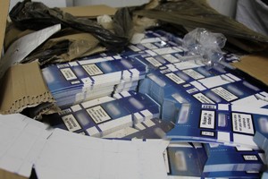 Na zdjęciu w rozerwanym kartonie widoczne są biało-niebieskie rozłożone kartoniki służące do produkcji opakowań do papierosów