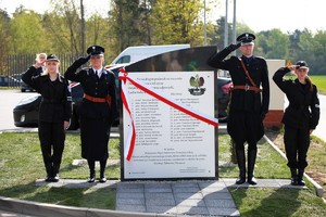 Pamiątkowy obelisk z biało-czerwoną szarfą, po obu stronach stoją policjant i policjantka w mundurach z 20-lecia międzywojennego i uczeń i uczennica z klasy mundurowej.