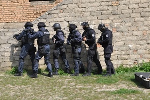 Sześciu policjantów w czarnych mundurach ćwiczebnych z uzbrojeniem stoi pod ścianą budynku