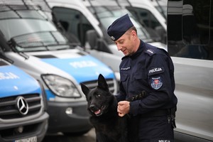 Policjant w mundurze bawi się ze swoim psem - pies stoi na tylnych łapach.
