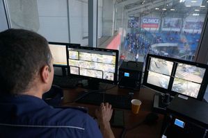 na zdjęciu umundurowany policjant na wieży widokowej, obserwujący monitoring stadionowy