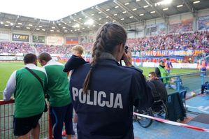 na zdjęciu umundurowana policjantka zespołu prasowego, fotografująca stadion