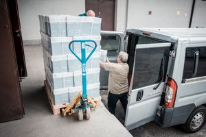 rampa magazynowa, paleta z papierem komputerowym - pracownicy ładują pudełka z papierem do samochodu dostawczego