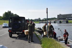 żołnierze wypakowują pakunki z samochodu wojskowego i przekazują je na łódke