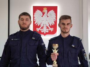 Dwaj policjanci z pucharem. W tle godło Polski.