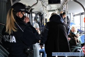 Zdjęcie przedstawia wnętrze autobusu z pasażerami, w środku znajduje się policjantka w mundurze oraz pracownik MPK