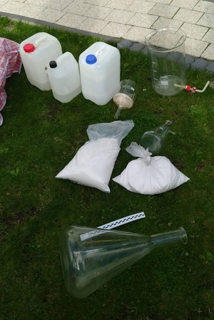 opakowania foliowe z zawartościa białej substancji,  plastikowe pojemniki-butelki z płynna zawartością, szklane menzurki , leżace na trawie