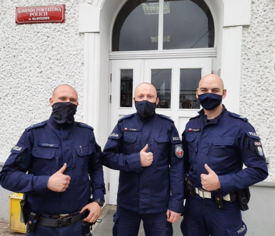 trzej policjanci z maseczkami na twarze stoją na tle budynku komendy policji