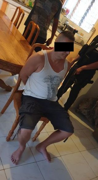 zatrzymany mężczyzna siedzi na krześle w pomieszczeniu, obok widać funkcjonariuszy Policji
