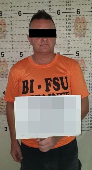 zatrzymany mężczyzna w pomarańczowej koszulce stoi i trzyma w lewej ręce przed sobą białą tablicę