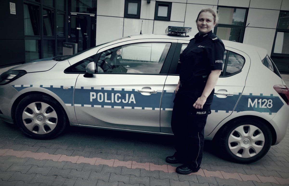 policjantka stoi przy radiowozie, z tyłu widoczny budynek Policji