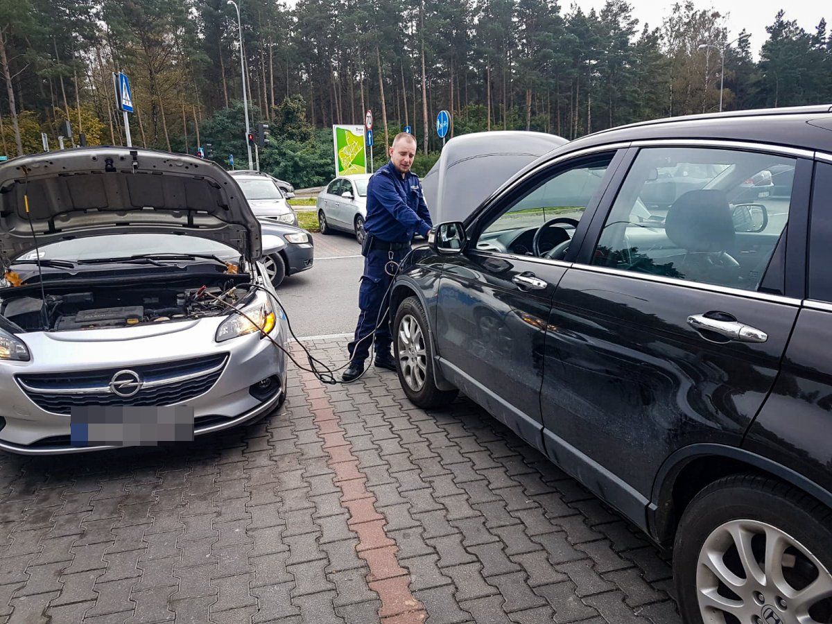 umundurowany policjant podpina kable z jednego samochodu do drugiego