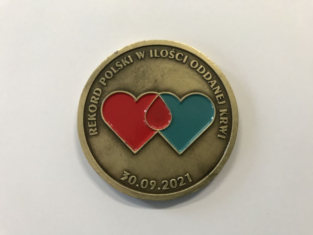 pamiątkowy medal z napisem rekord Polski w ilości oddanej krwi 30.09.2021 r. Na środku znajdują się dwa serca czerwone i niebieskie