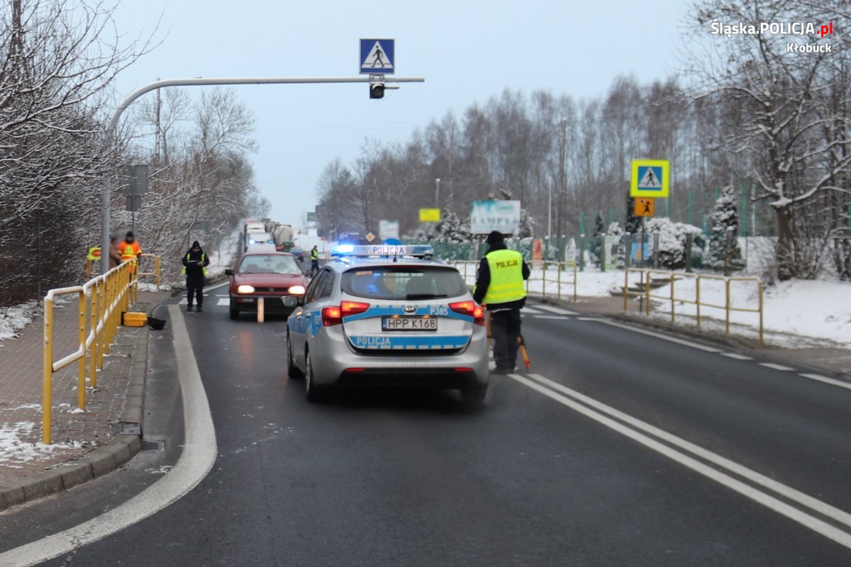 Na ulicy stoi radiowóz, przed samochodem, który brał udział w wypadku, obok stoi umundurowany policjant