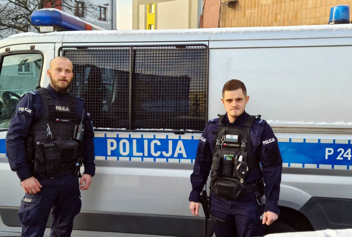 dwaj policjanci stoją przed radiowozem policyjnym