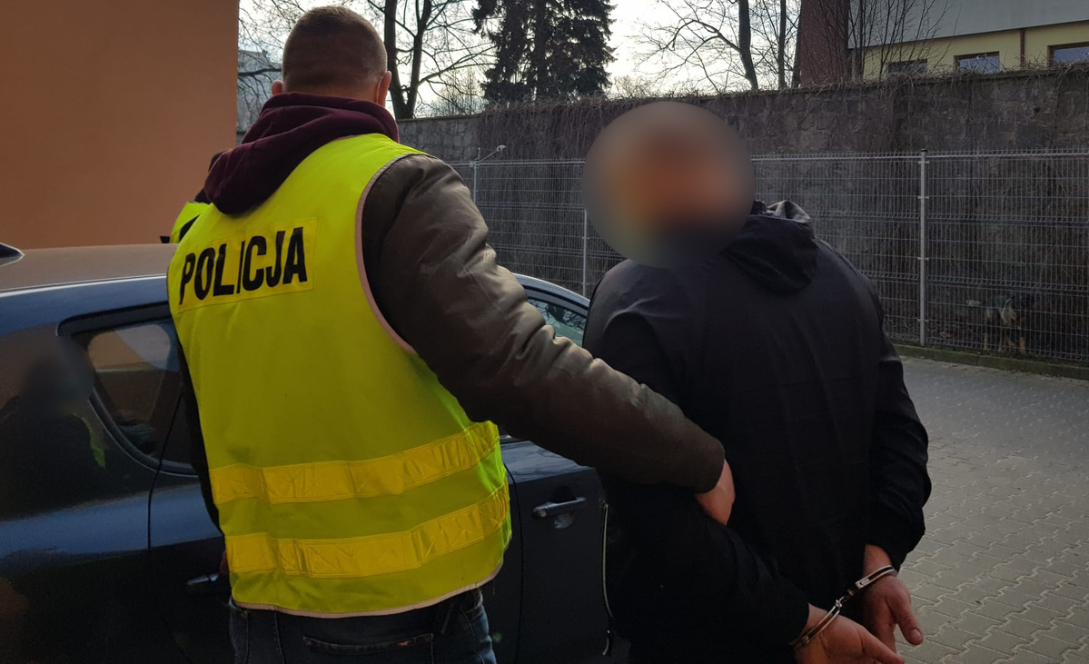 policjant prowadzi do radiowozu zatrzymanego mężczyznę
