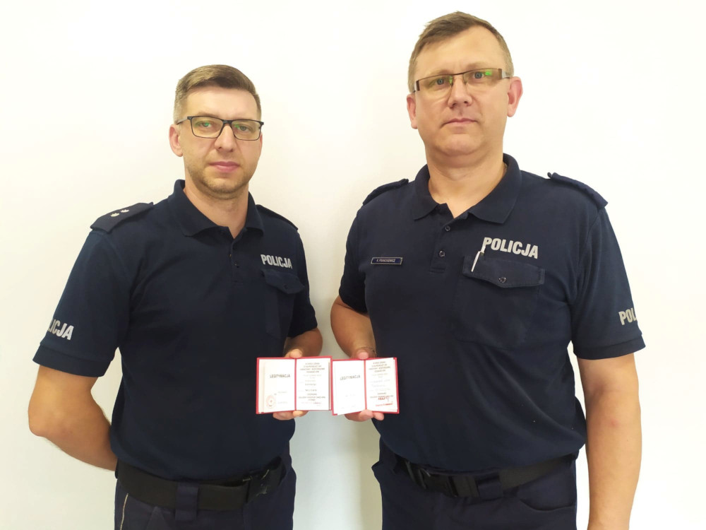 dwaj policjanci trzymają przed sobą legitymacje Złotej odznaki „ Zasłużony Dawca Krwi I Stopnia”