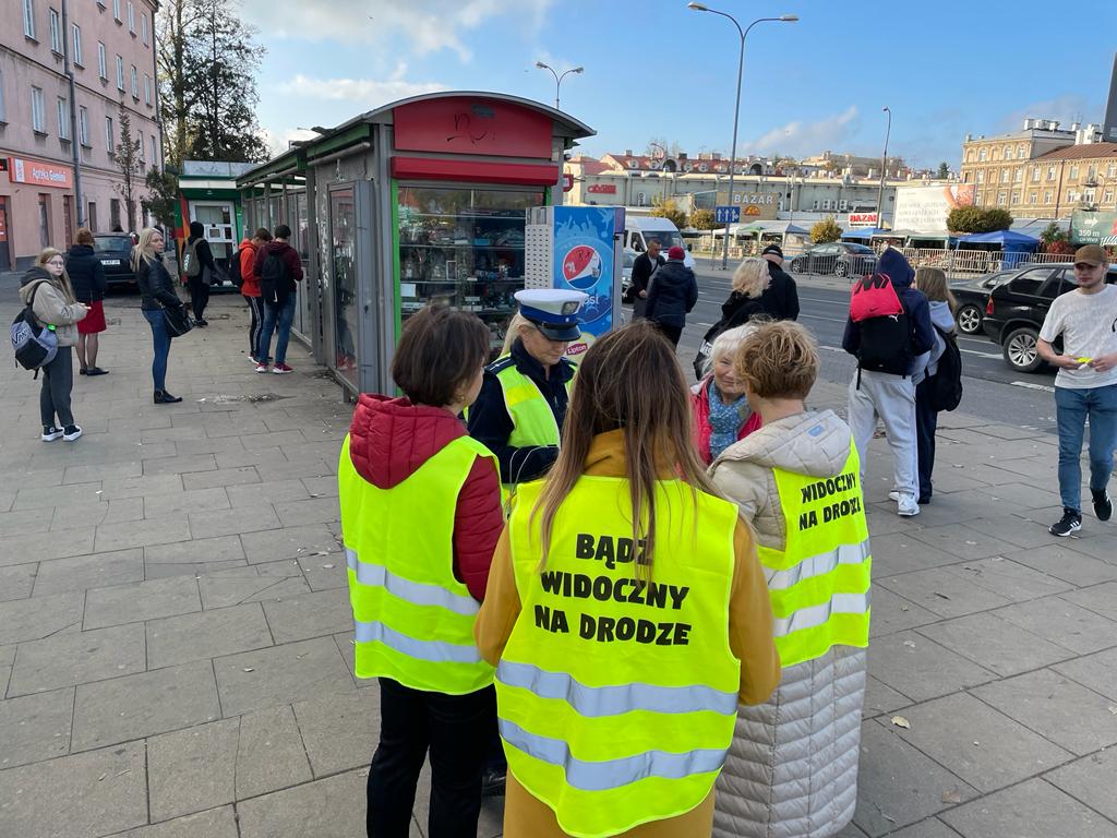 umundurowana policjantka i pracownice WORD w odblaskowych kamizelkach na przystanku autobusowym rozdają ludziom odblaski