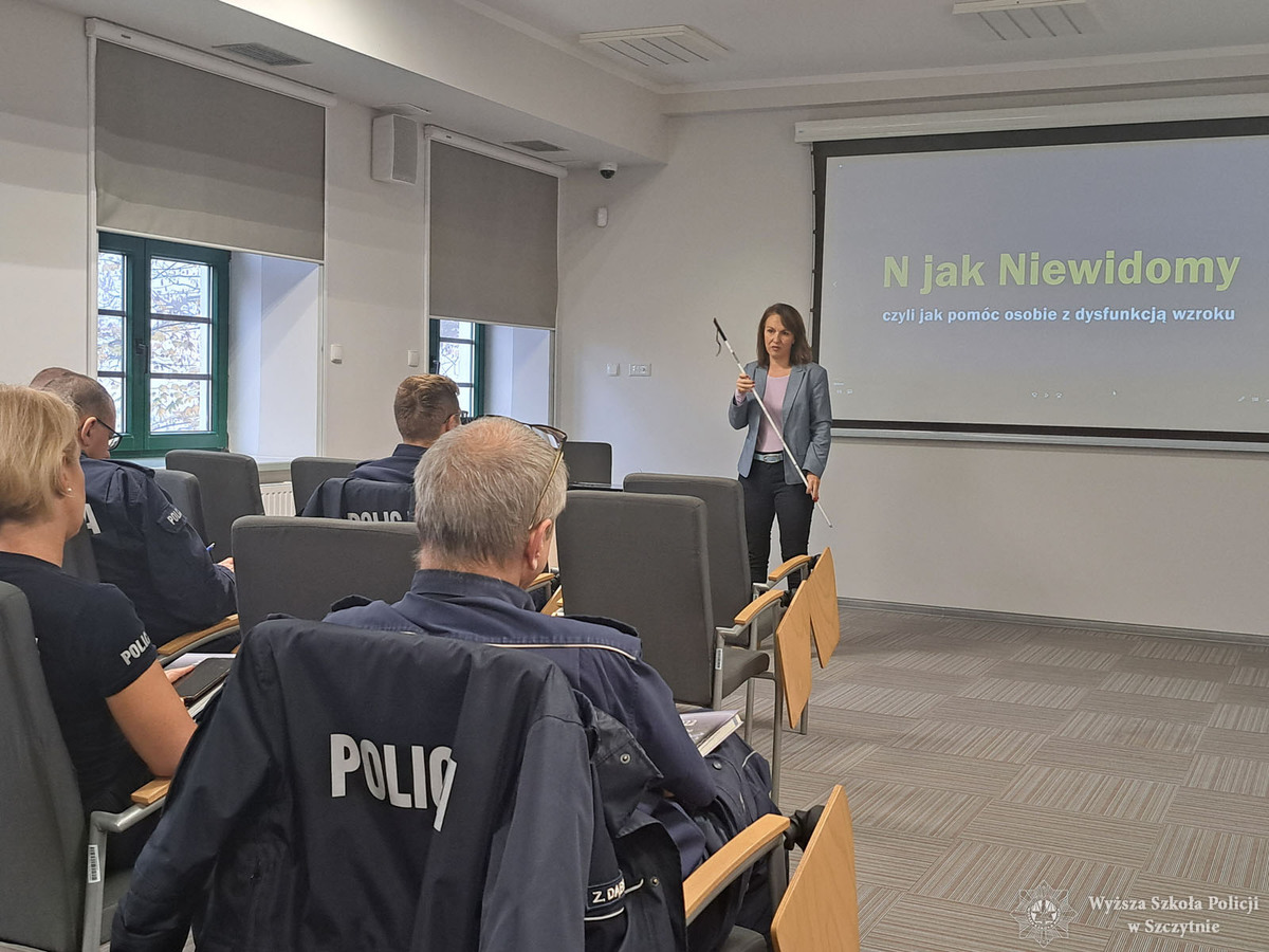 policjanci podczas szkolenia. Prowadząca stoi na przeciwko nich i trzyma w ręku białą laskę