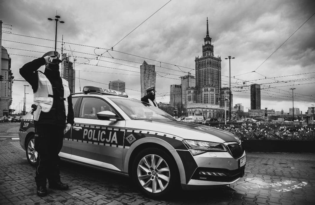 Zdjęcie czarno-białe. Policjant stoi przy radiowozie policyjnym
